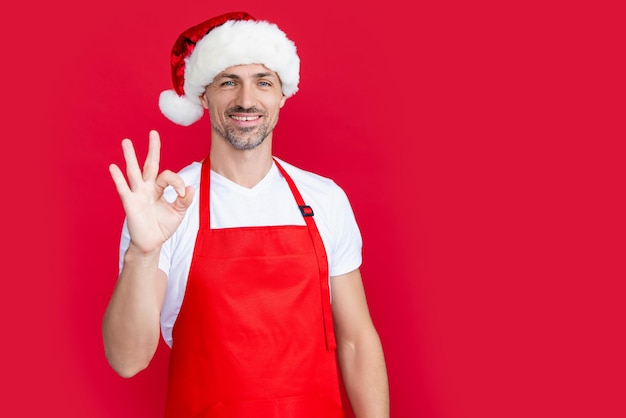 Hombre maduro alegre con delantal de barista rojo y gorro de Papá Noel navideño