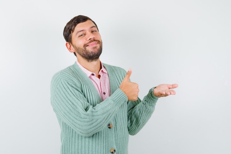 Foto hombre maduro en camisa, cardigan mostrando el pulgar hacia arriba, extendiendo la palma hacia un lado y mirando alegre, vista frontal.
