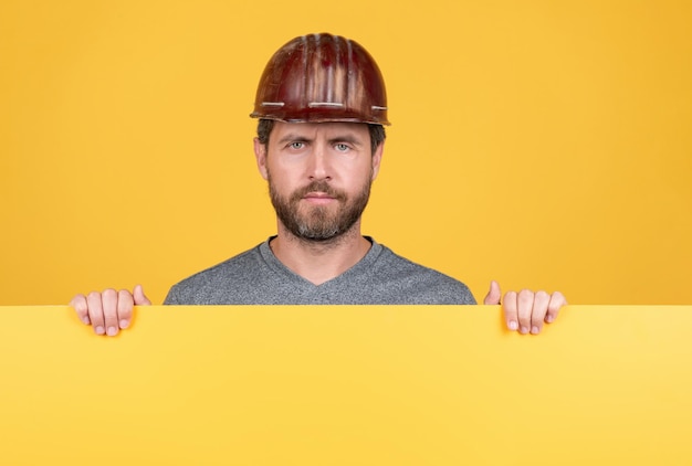 Hombre maduro con casco. constructor con espacio de copia en papel. presentando información novedosa. trabajador barbudo con casco detrás de una hoja de papel amarilla. publicidad obrera. anuncio. feliz Día del Trabajo.