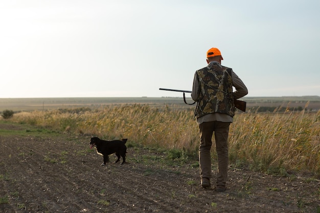 Foto hombre maduro cazador con arma mientras camina en el campo con sus perros