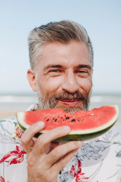 Foto hombre maduro comiendo sandía en la playa