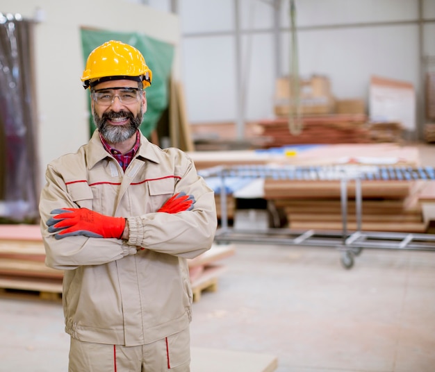 Hombre maduro confiado de pie con los brazos cruzados en la unidad de fabricación de fábrica con casco naranja