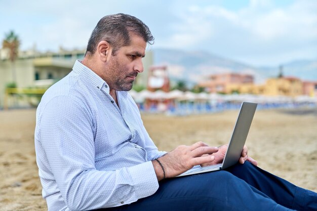 Hombre maduro confiado serio con la computadora portátil al aire libre