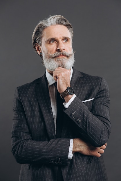 Hombre maduro elegante y de moda en un traje gris con barba y pensamiento. Concepto de primer plano empresarial y moderno en la pared gris