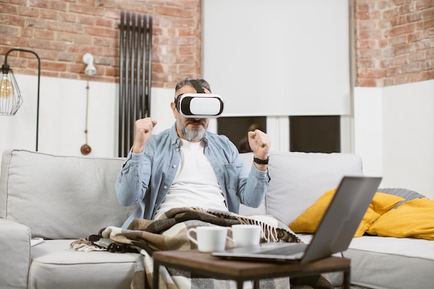 Hombre maduro emocionado sentado en un sofá con gafas VR