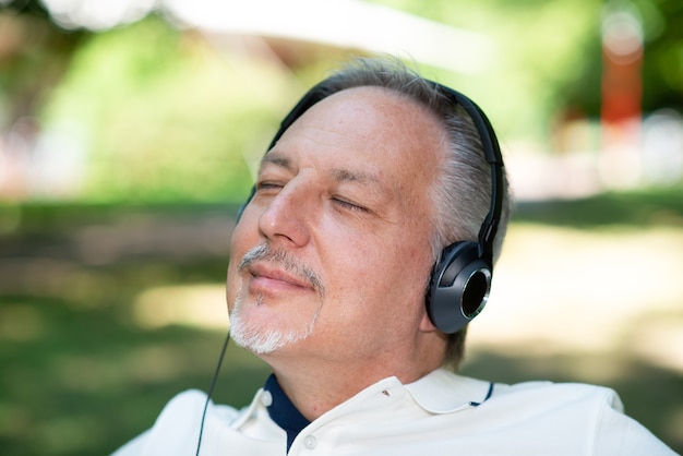 Hombre maduro, escuchando música en un parque con los ojos cerrados