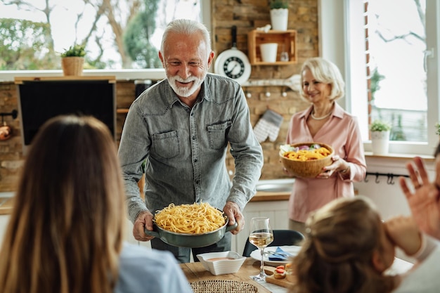 Hombre maduro feliz almorzando en familia y trayendo comida a la mesa