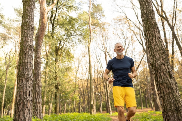 Hombre maduro feliz disfrutando corriendo por el bosque