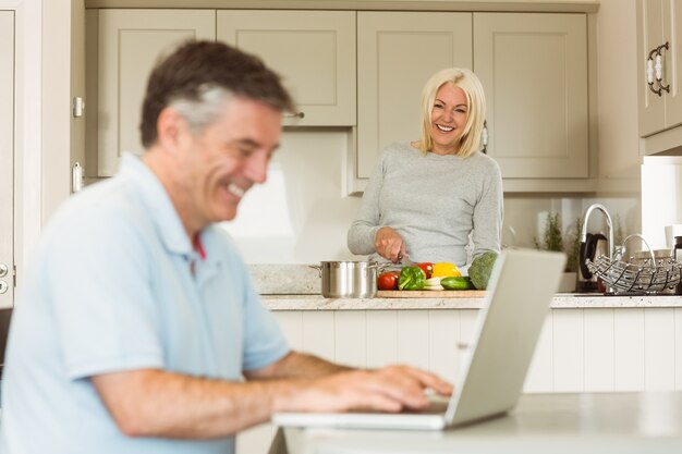 Hombre maduro feliz que usa la computadora portátil mientras que la esposa prepara vehículos