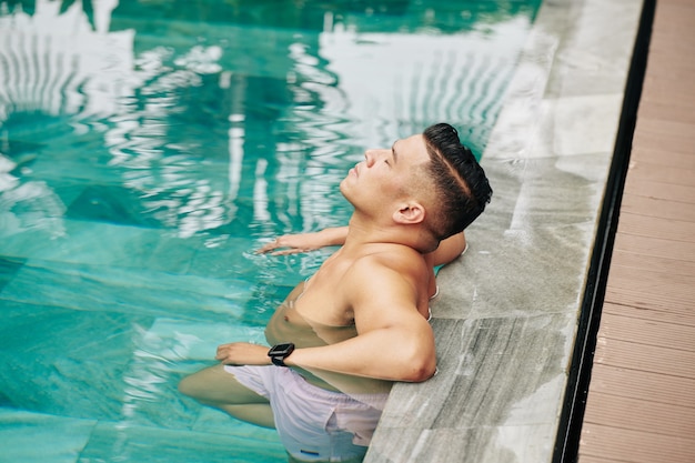 Hombre maduro en forma relajante y refrescante en la piscina en un caluroso día de verano