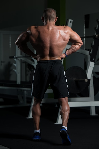 Hombre maduro guapo de pie fuerte en el gimnasio y flexionando los músculos Muscular culturista atlético Fitness masculino posando después de los ejercicios