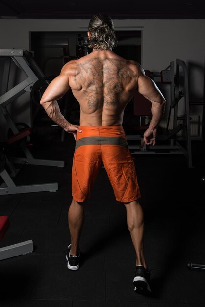Hombre maduro guapo de pie fuerte en el gimnasio y flexionando los músculos Muscular culturista atlético modelo de fitness posando después de los ejercicios