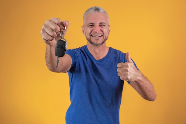 Hombre maduro guapo sonriendo sosteniendo una llave de auto feliz con el pulgar hacia arriba