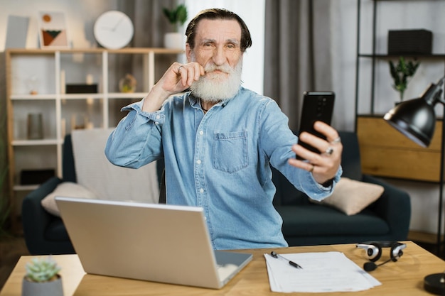 Hombre maduro joven feliz sonriendo y gesticulando durante la videollamada en un teléfono inteligente moderno