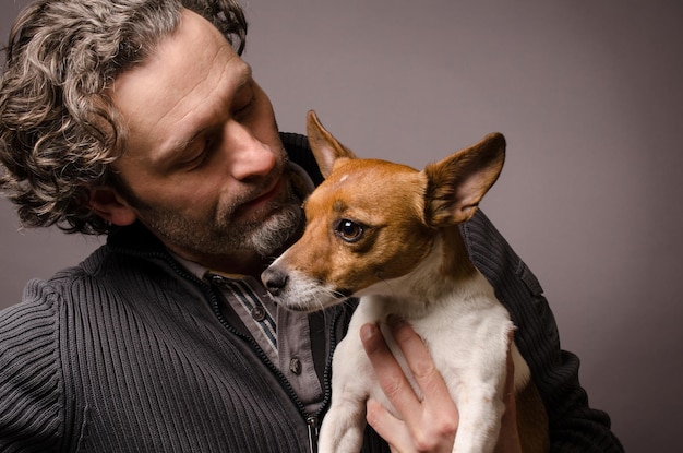 Hombre maduro llevando un Jack Russell Terrier contra un fondo gris