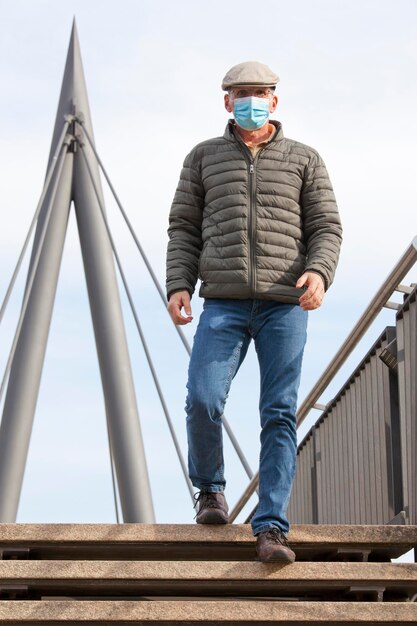 Hombre maduro con máscara facial caminando por un puente peatonal en una ciudad - céntrate en el hombre