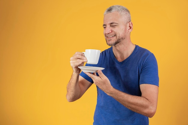 Hombre maduro de mediana edad tomando un café o té con fondo amarillo con espacio libre para texto