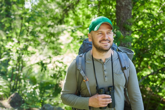 Hombre maduro con mochila a la espalda y binoculares feliz con su viaje en el bosque