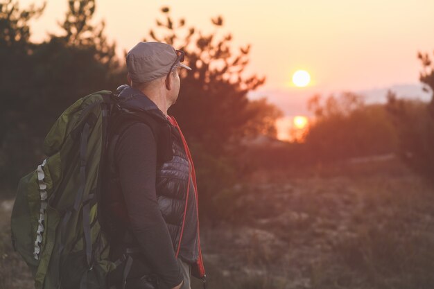 Hombre maduro con mochila en la tapa mirar el atardecer en el bosque