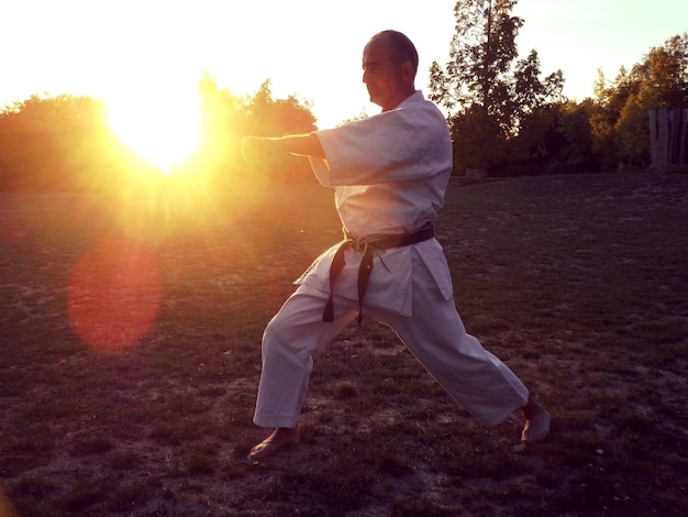 Hombre maduro practicando karate mientras está de pie en el campo contra el cielo durante la puesta de sol