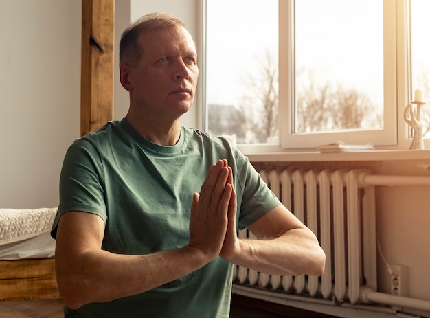 Hombre maduro, practicar yoga y meditar en casa acogedora con las manos juntas