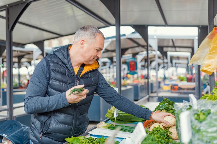 Foto hombre maduro recogiendo verduras en el mercado de los agricultores.