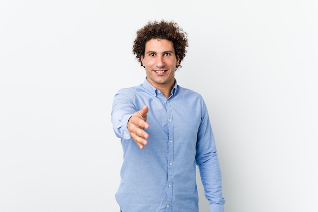 Hombre maduro rizado joven que lleva una camisa elegante que estira la mano en la cámara en gesto de saludo.