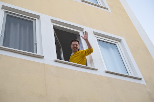 Hombre maduro saludando con la mano saludando a su amigo desde la ventana