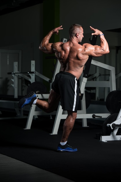 Hombre maduro sano de pie fuerte en el gimnasio y flexionando los músculos Muscular culturista atlético Fitness masculino posando después de los ejercicios