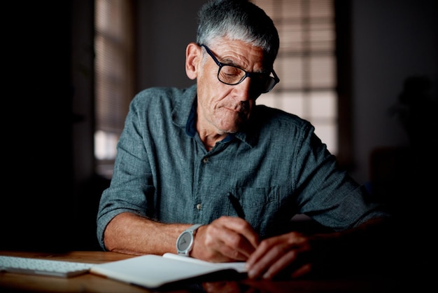 Hombre maduro serio y la escritura de notas de noche y trabajar hasta tarde en la oficina de casa empresario y gafas lectura de visión y cuaderno para la planificación de la persona tormenta de ideas y CEO de pequeñas empresas
