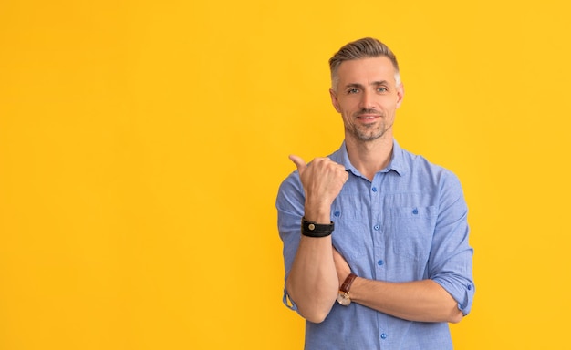 Hombre maduro sonriente con cabello canoso muestra el pulgar hacia arriba en el espacio de copia de fondo amarillo señalando con el dedo
