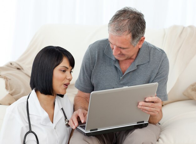 Hombre maduro con su enfermera mirando la computadora portátil en casa