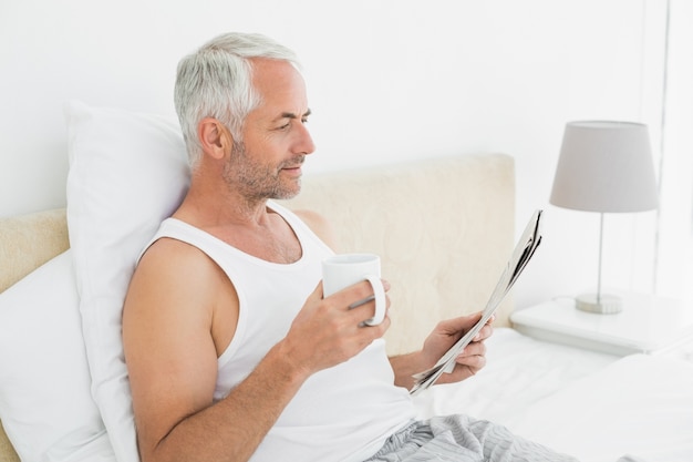 Hombre maduro con taza de café y periódico en la cama