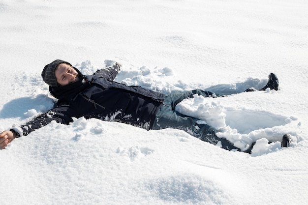 El hombre maduro yace en la nieve blanca y esponjosa y se ríe. Vacaciones de invierno.