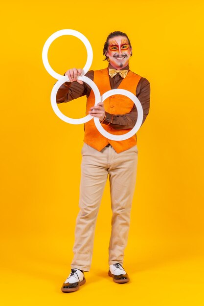 Hombre malabarista feliz en chaleco de maquillaje haciendo malabares con aros sobre un fondo amarillo