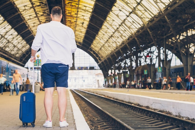 Hombre con maleta sobre ruedas de pie en la plataforma de la estación de tren