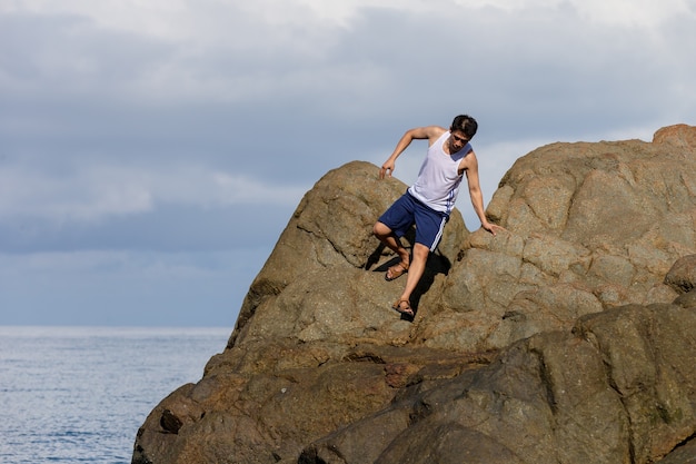 Hombre de mañana ejercicio con gran escalada en roca junto al mar.