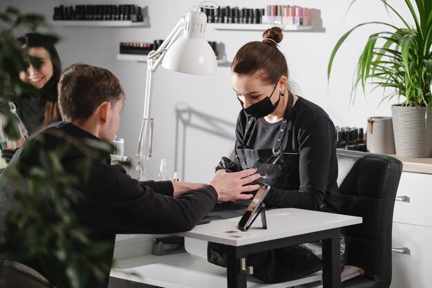 Hombre manicure mujer maestro de servicio de uñas haciendo manicure para el hombre