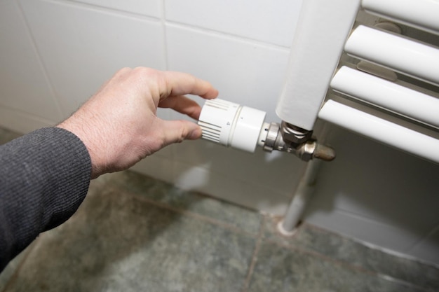 Hombre de mano ajustando el termostato doméstico en el radiador de calefacción blanco