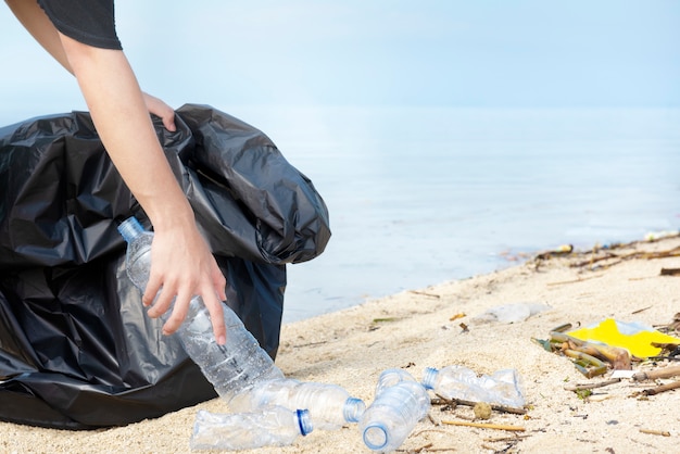 Hombre de mano con bolsa de basura recogiendo botellas de plástico en la playa