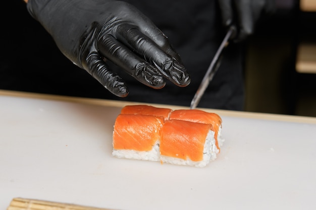 Hombre mano cortando con cuchillo rollos de salmón