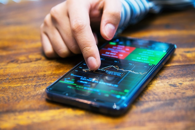 Hombre de la mano y gráfico del mercado de valores en la pantalla del móvil.