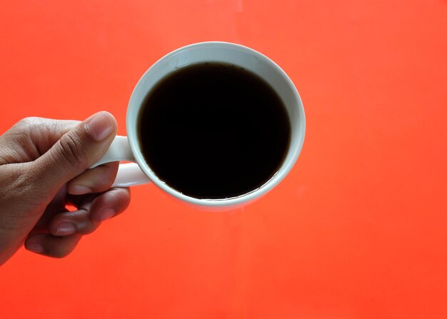 Foto hombre con la mano sosteniendo una taza blanca de café negro aislado sobre un fondo naranja.