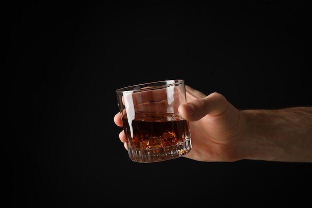 Hombre mano sostiene un vaso de whisky sobre fondo negro, espacio para texto