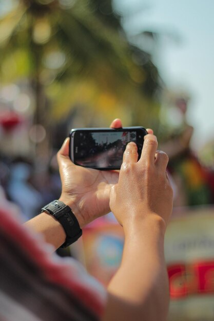 Foto hombre con una mano usando un teléfono inteligente tomando fotos en la calle durante la celebración del ponorogo