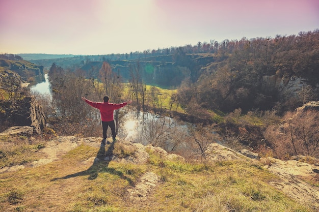 Un hombre con las manos en el aire sobre una piedra sobre un hermoso cañón en un soleado día de otoño