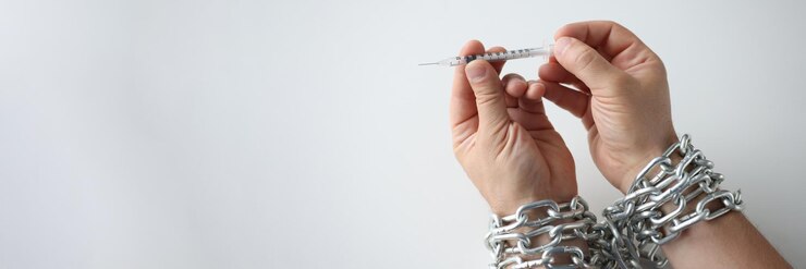 Foto hombre con las manos atadas con una cadena de metal sosteniendo una jeringa con drogas de cerca