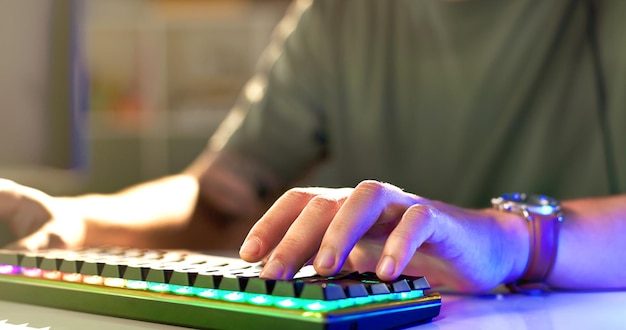 Hombre manos y jugador con teclado de neón para partido de esports o torneo en línea en el escritorio en casa Persona masculina o streamer de primer plano con equipos periféricos o informáticos para desafío o juego