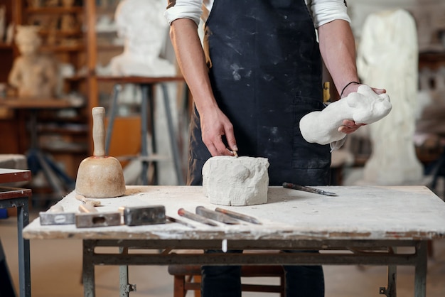 Hombre manos trabajando con una piedra blanca. El escultor profesional talla escultura de piedra caliza.