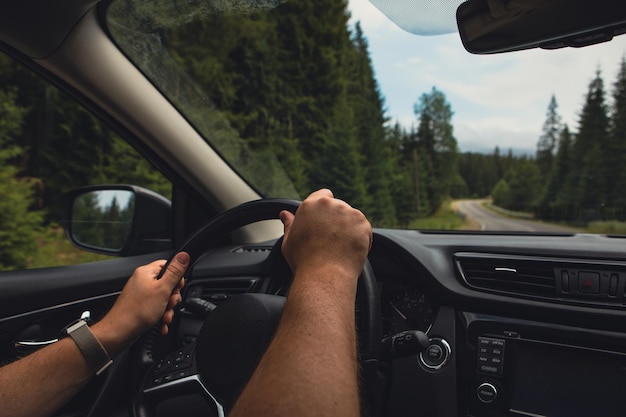 Foto hombre con las manos en el volante conduciendo un coche por la carretera de las montañas